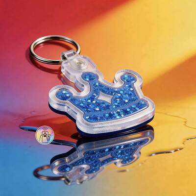 Clear acrylic pet ID tag shaped like a crown with blue glitter, attached to a keyring — Shiloh's House smart NFC pet tag with free companion Lohji app.