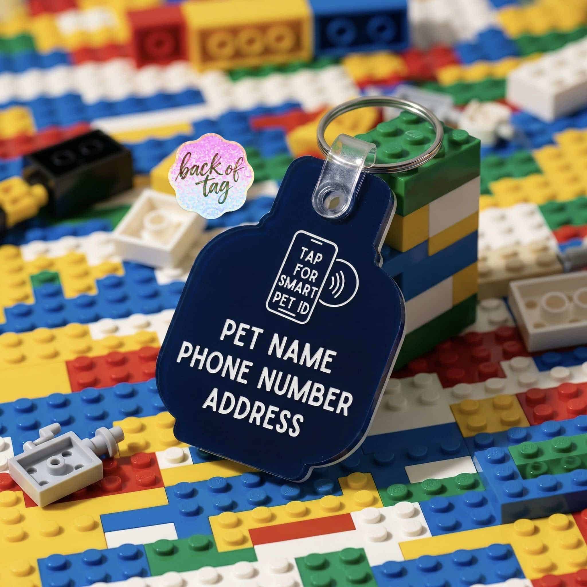 NFC pet ID tag in blue with space for pet's name, phone, and address, on colorful LEGO background — Shiloh's House smart NFC pet tag with free companion Lohji app.