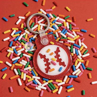 Bright red pet ID tag with a spooky face, surrounded by colorful sprinkles on a red background — Shiloh's House smart NFC pet tag with free companion Lohji app.