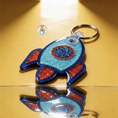 NFC pet ID tag shaped like a rocket with glittery blue and red acrylic, attached to a keyring, on a.