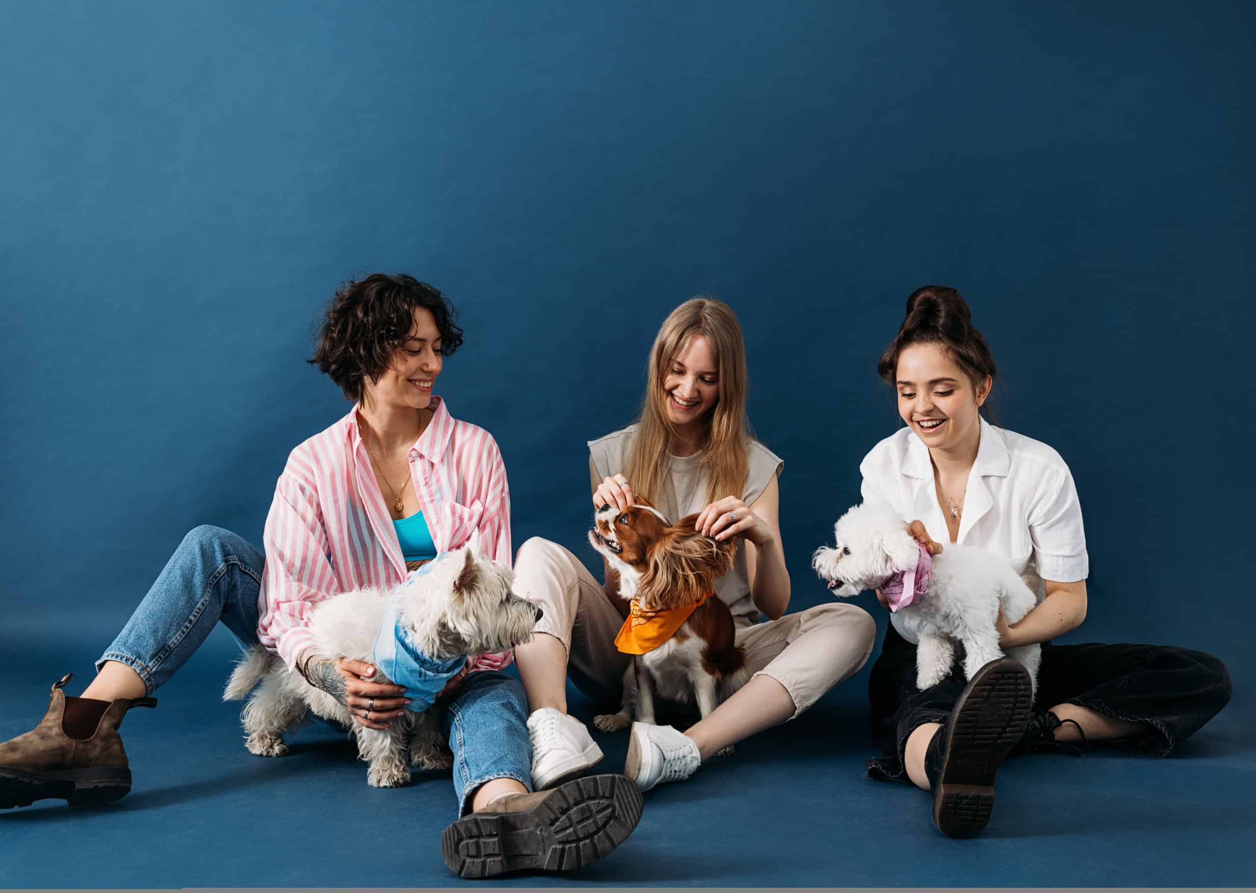 Three happy women sitting with their well-trained dogs — trained with high-value treats