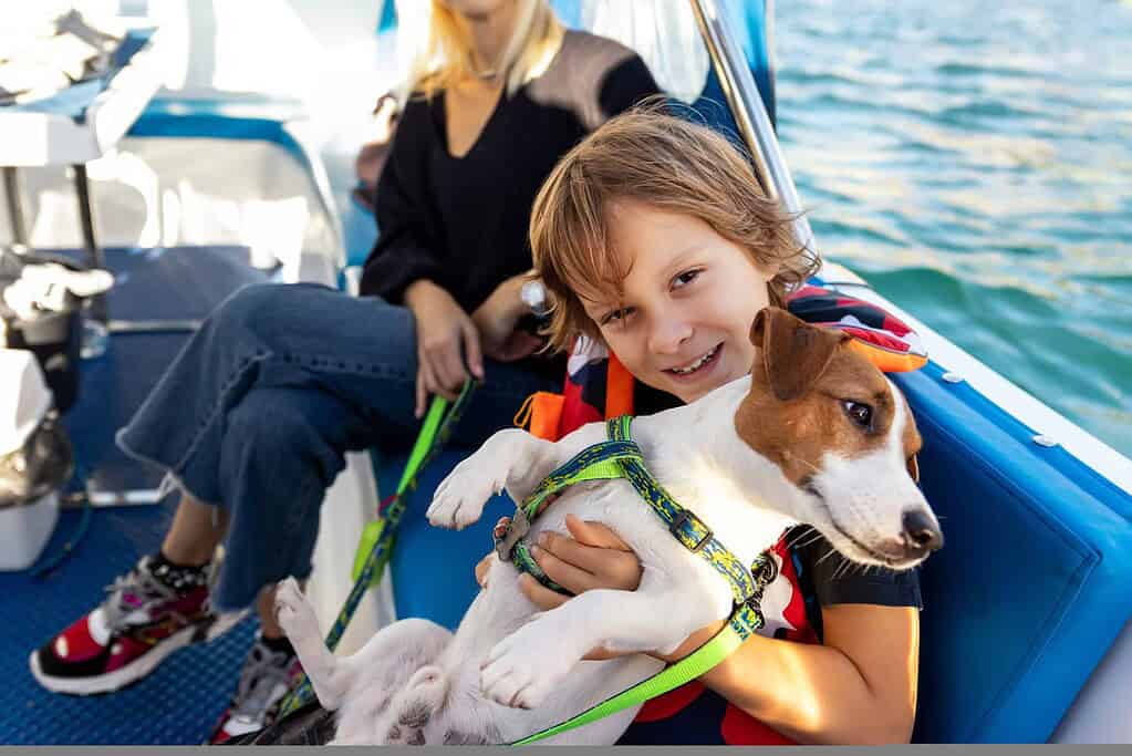 Child holding a dog on a boat with water in the background.
