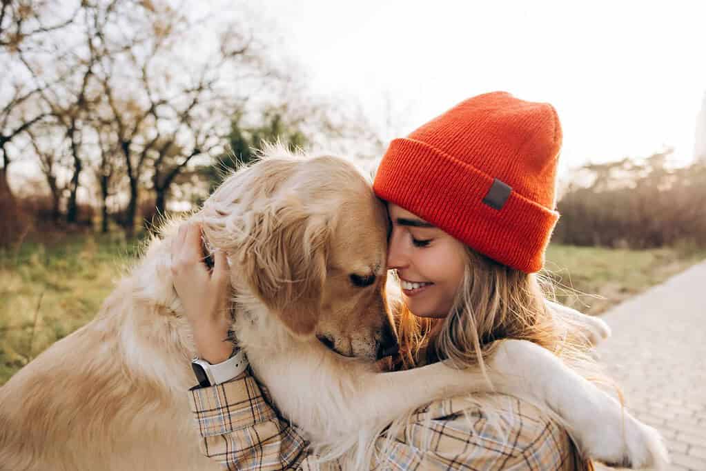 Woman in red beanie hugging golden retriever in park.