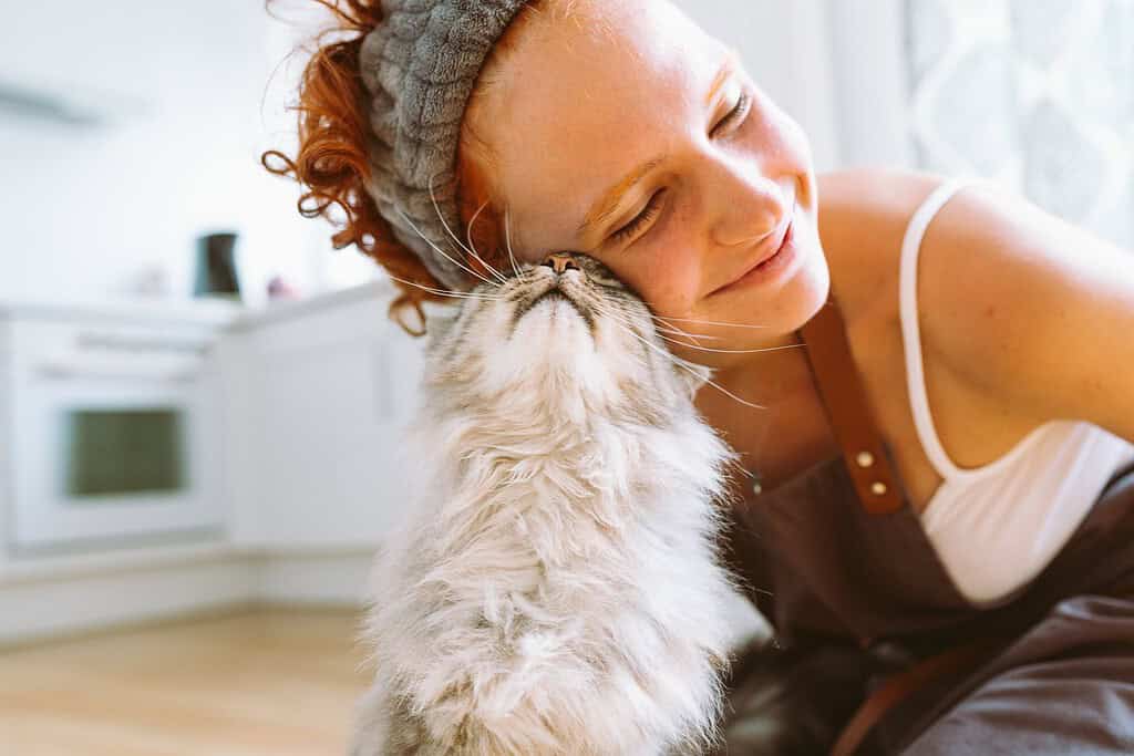 Smiling woman cuddling a fluffy cat in a bright kitchen.