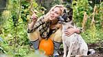 Woman kneeling with her dog beside a pumpkin in an autumn garden