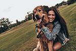 Smiling woman hugging a large long-haired golden-brown dog on a grassy hillside